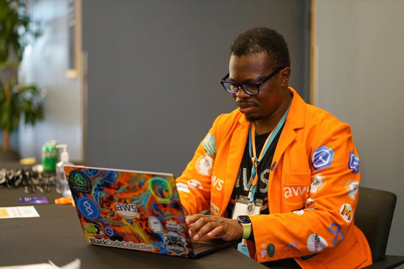 Banjo coding on his sticker-covered laptop in an orange AWS jacket